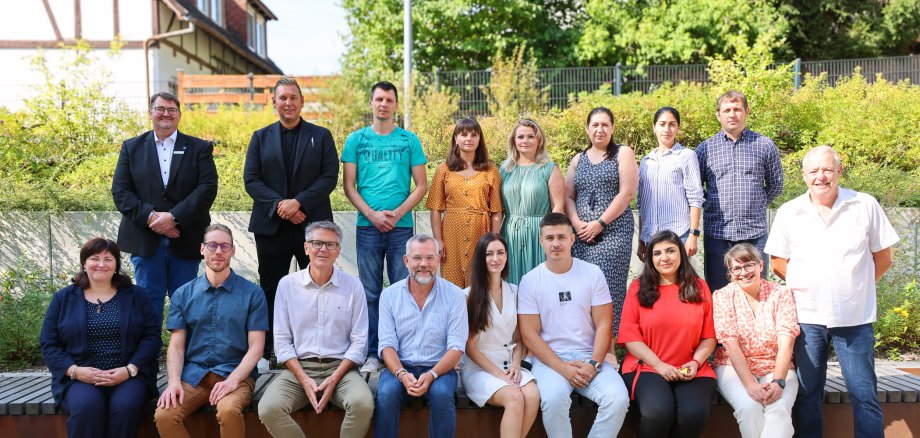 Gruppenfoto vor der Kreisverwaltung Hersfeld-Rotenburg mit Bundestagsabgeordnetem Michael Roth, Projektkoordinatoren und Teilnehmenden der Integrationsprojekte WIR-ONnFIT und LIMEA-MY TURN. Im Hintergrund ist ein Gebäude mit Fachwerk zu sehen, im Vordergrund sitzen und stehen 16 Personen auf einer Bank und Stufen im Freien.
