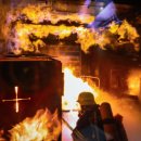 Ein Feuerwehrmann in voller Schutzausrüstung mit Atemschutzgerät befindet sich in einem brennenden Raum. Über ihm schlagen helle Flammen an der Decke entlang, dichter Rauch steigt auf. Die Szene zeigt eine realistische Trainingssituation zur Brandbekämpfung in einer mobilen Brandsimulationsanlage.