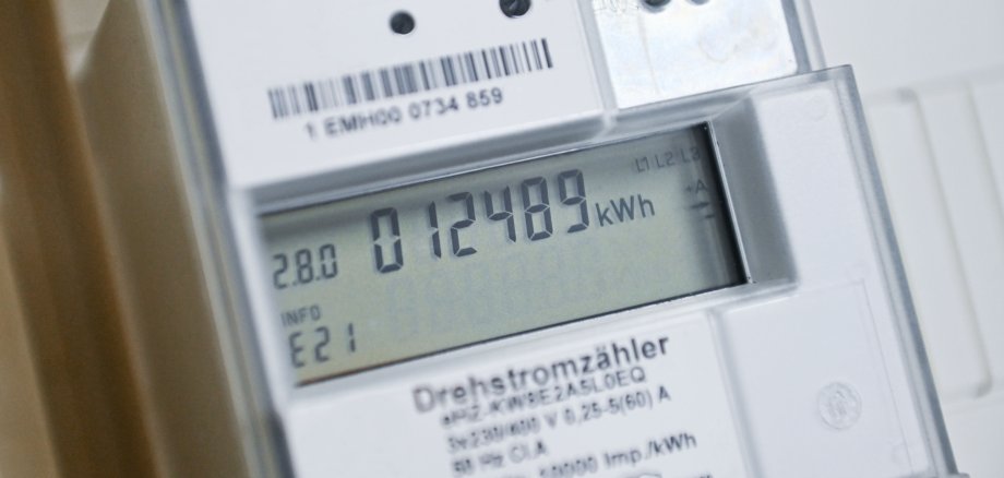 Ein digitaler Stromzähler zeigt einen Verbrauch von 012489 kWh auf seinem Display. Oberhalb des Displays sind ein Barcode und weitere technische Details sichtbar.