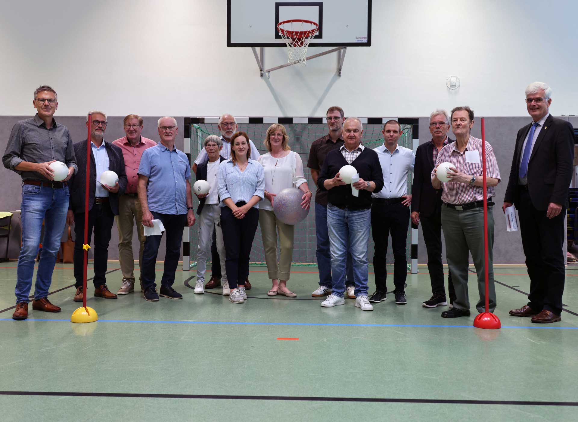 Gruppenfoto von Kreisausschussmitgliedern in der Turnhalle unter einem Basketballkorb, einige halten Bälle in der Hand.