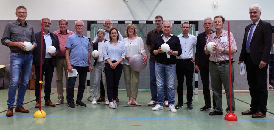 Gruppenfoto von Kreisausschussmitgliedern in der Turnhalle unter einem Basketballkorb, einige halten Bälle in der Hand.