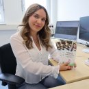 Eine junge Frau sitzt an einem Schreibtisch mit zwei Monitoren und hält mehrere Infoflyer mit dem Titel „Verfahrenslotsin im Landkreis Hersfeld-Rotenburg“ in der Hand. Sie blickt freundlich in die Kamera.