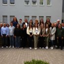 Eine große Gruppe steht in zwei Reihen für ein Gruppenfoto im Innenhof des Landratsamts. Im Hintergrund ist ein graues Gebäude mit Fenstern zu sehen. Die Personen lächeln in die Kamera.