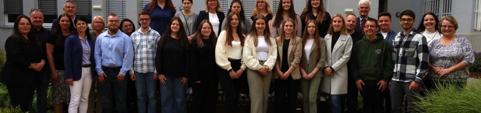 Eine große Gruppe steht in zwei Reihen für ein Gruppenfoto im Innenhof des Landratsamts. Im Hintergrund ist ein graues Gebäude mit Fenstern zu sehen. Die Personen lächeln in die Kamera.