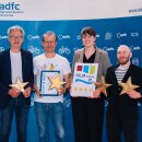 Vier Personen stehen vor einer blauen ADFC-Fotowand und halten Urkunden sowie goldene Sterne in den Händen. Eine Frau hält zudem ein Schild mit dem Logo und vier Sternen des Fulda-Radwegs R1.