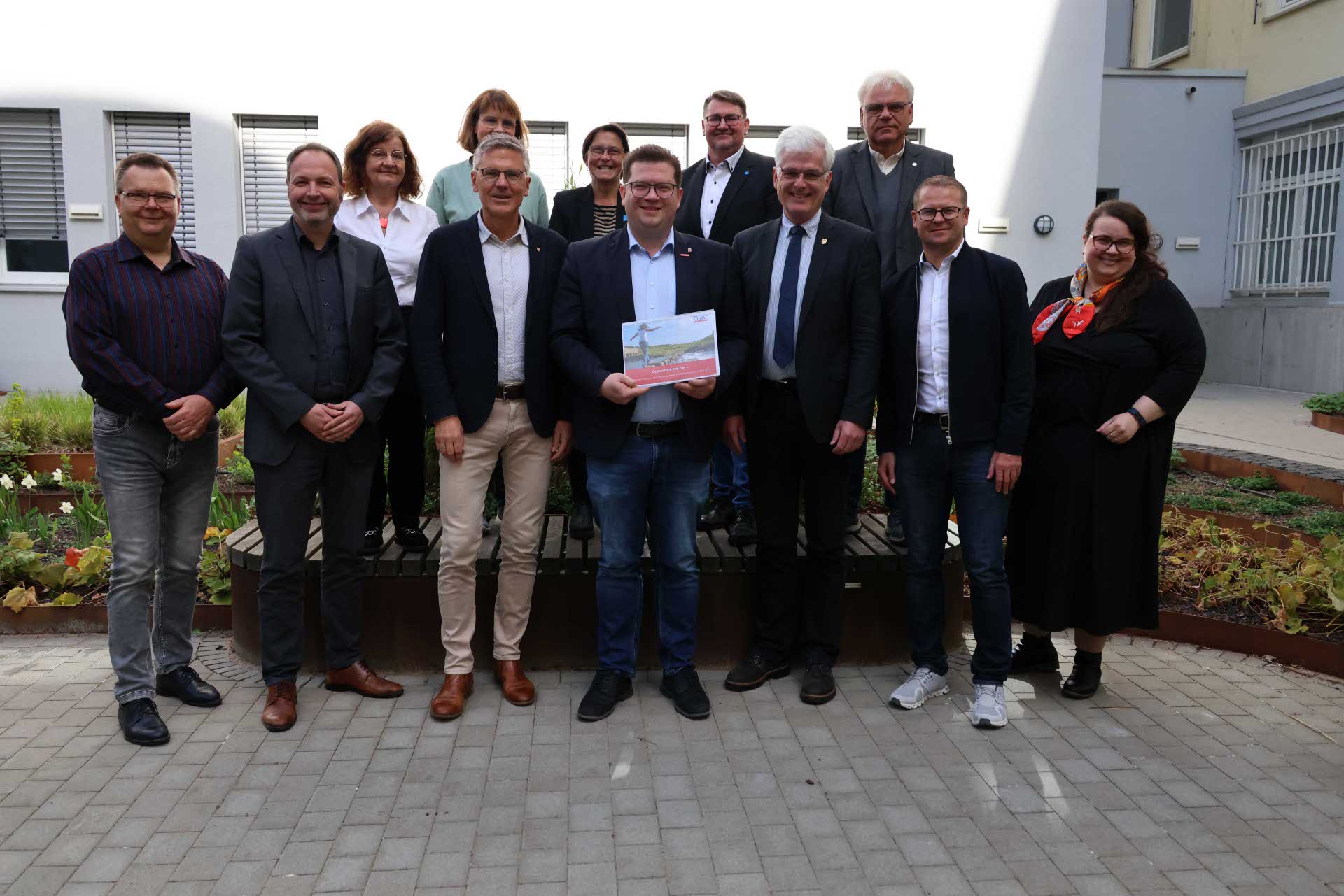 Eine Gruppe von 15 Personen steht im Innenhof eines Verwaltungsgebäudes, in der Mitte hält ein Mann ein Dokument mit dem Titel der OloV-Strategie. Es handelt sich um Vertreterinnen und Vertreter aus Kreisverwaltung, Wirtschaft, Schulen und Verbänden, die sich gemeinsam für die berufliche Orientierung von Jugendlichen im Landkreis Hersfeld-Rotenburg einsetzen.
