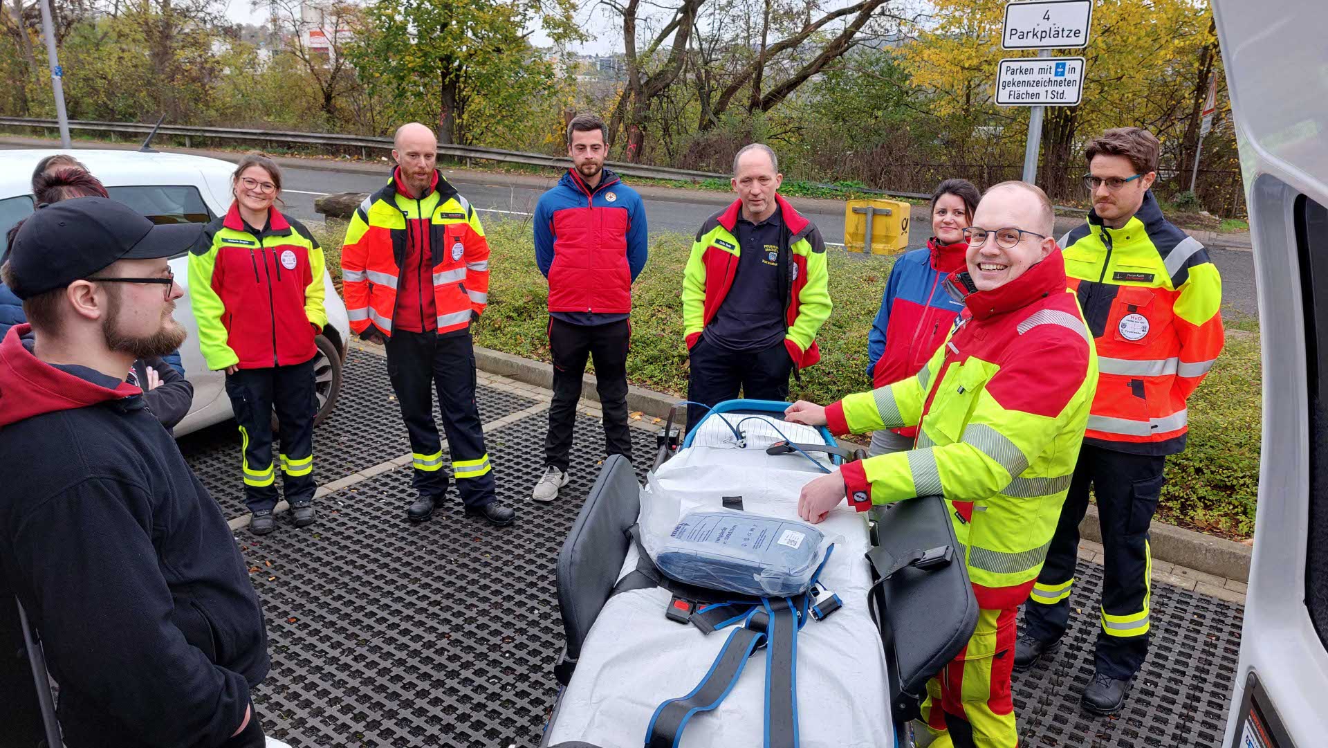 Mehrere ehrenamtliche Einsatzkräfte in Rettungsdienstkleidung stehen im Freien um eine Trage und besprechen gemeinsam ein Einsatzszenario während einer Fortbildung.