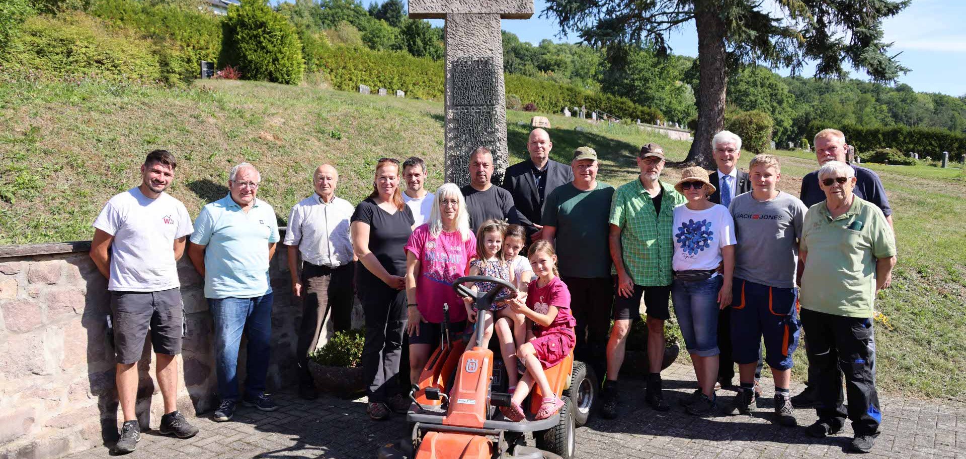 Eine Gruppe von Menschen steht auf dem Friedhof in Rohrbach. Im Vordergrund sieht man einen Sitz-Rasenmäher.