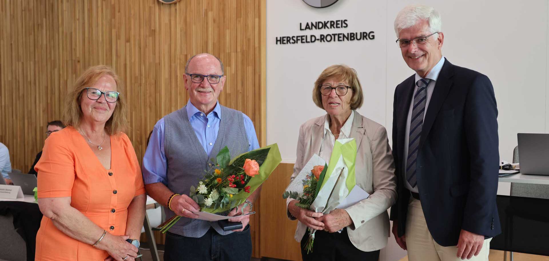 Zwei Männer und zwei Frauen schauen in die Kamera. Die beiden Personen in der Mitte halten einen Blumenstrauß in den Händen.