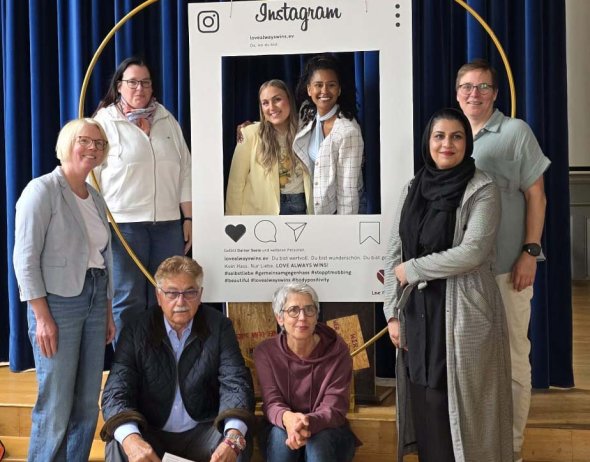 Eine Gruppe von Menschen steht auf einer Bühne für ein Gruppenbild. Sie sind um einen Papierrahmen mit der Aufschrift "Instagram" aufgestellt.