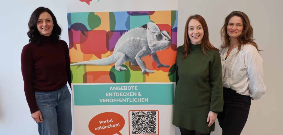 Drei Frauen stehen nebeneinander vor einem bunten Roll-up zum Bildungs- und Betreuungsportal des Landkreises Hersfeld-Rotenburg und lächeln in die Kamera.