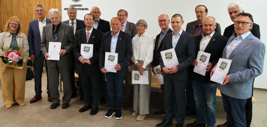 Gruppenfoto in einem Sitzungssaal: Mehrere Frauen und Männer stehen nebeneinander vor einer weißen Wand mit dem Wappen und der Aufschrift „Landkreis Hersfeld-Rotenburg“. Einige Personen halten Urkunden oder Mappen in den Händen, links im Bild hält eine Frau einen Blumenstrauß. Die Gruppe wirkt wie bei einer offiziellen Ehrung oder Auszeichnung fotografiert.