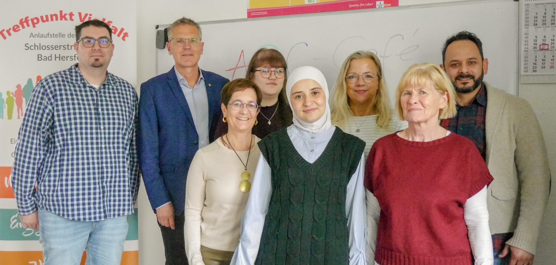 Acht Personen stehen gemeinsam für ein Gruppenfoto im ABC-Café im Treffpunkt Vielfalt in Bad Hersfeld vor einer beschrifteten Tafel. Die Gruppe setzt sich aus Mitarbeitenden und Beteiligten des Projekts zusammen.