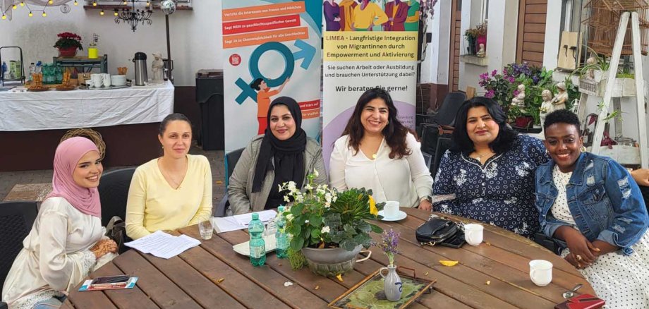 Einige Frauen sitzen an einem Tisch im Innenhof eines Gebäudes. Sie schauen alle freundlich in die Kamera.