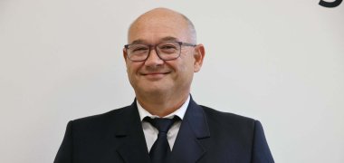 Portrait Martin Orf Martin Orf lächelt in dunkelblauer Feuerwehruniform und mit Brille vor einer hellen Wand in die Kamera.